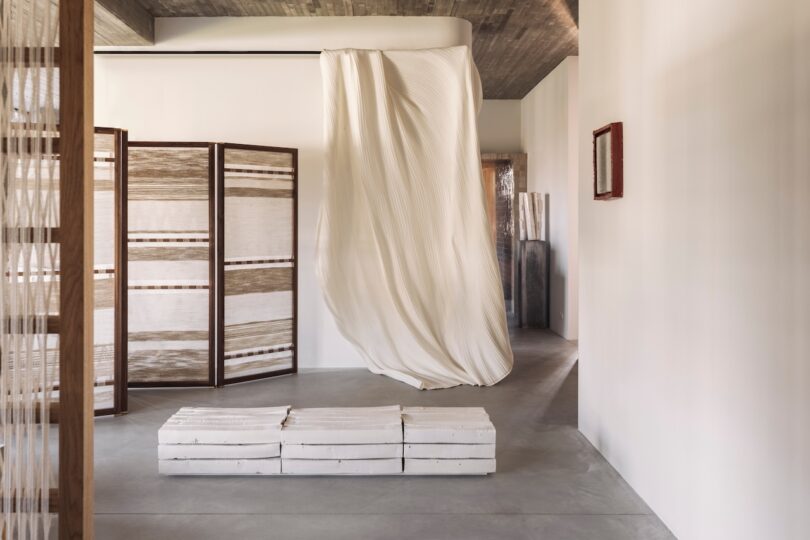 Minimalist interior featuring a long white pleated fabric suspended from the ceiling.