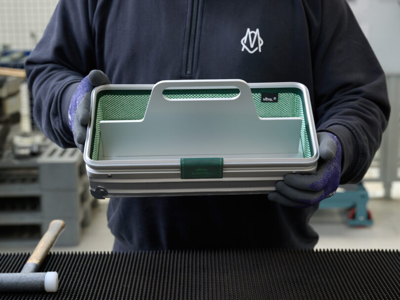 A person holding the silver aluminum toolbox with green accents in a creative workspace.