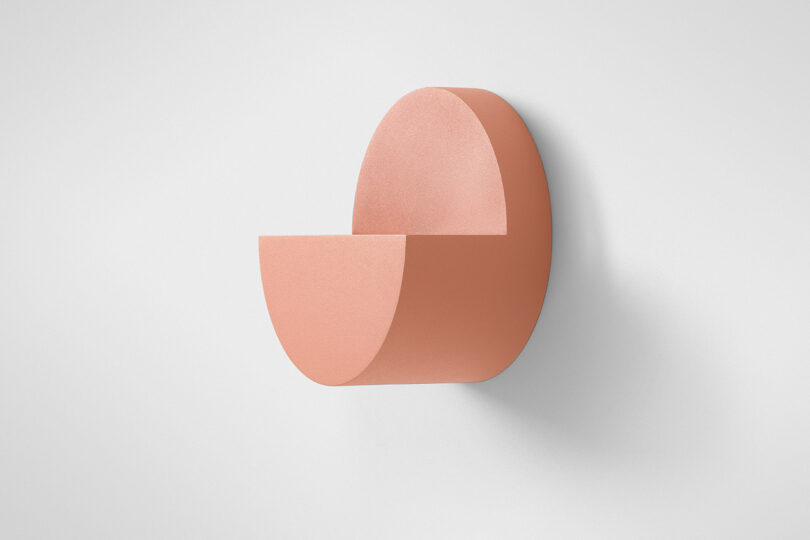 A minimalist semicircular salmon-pink wall fixture mounted on a white wall.
