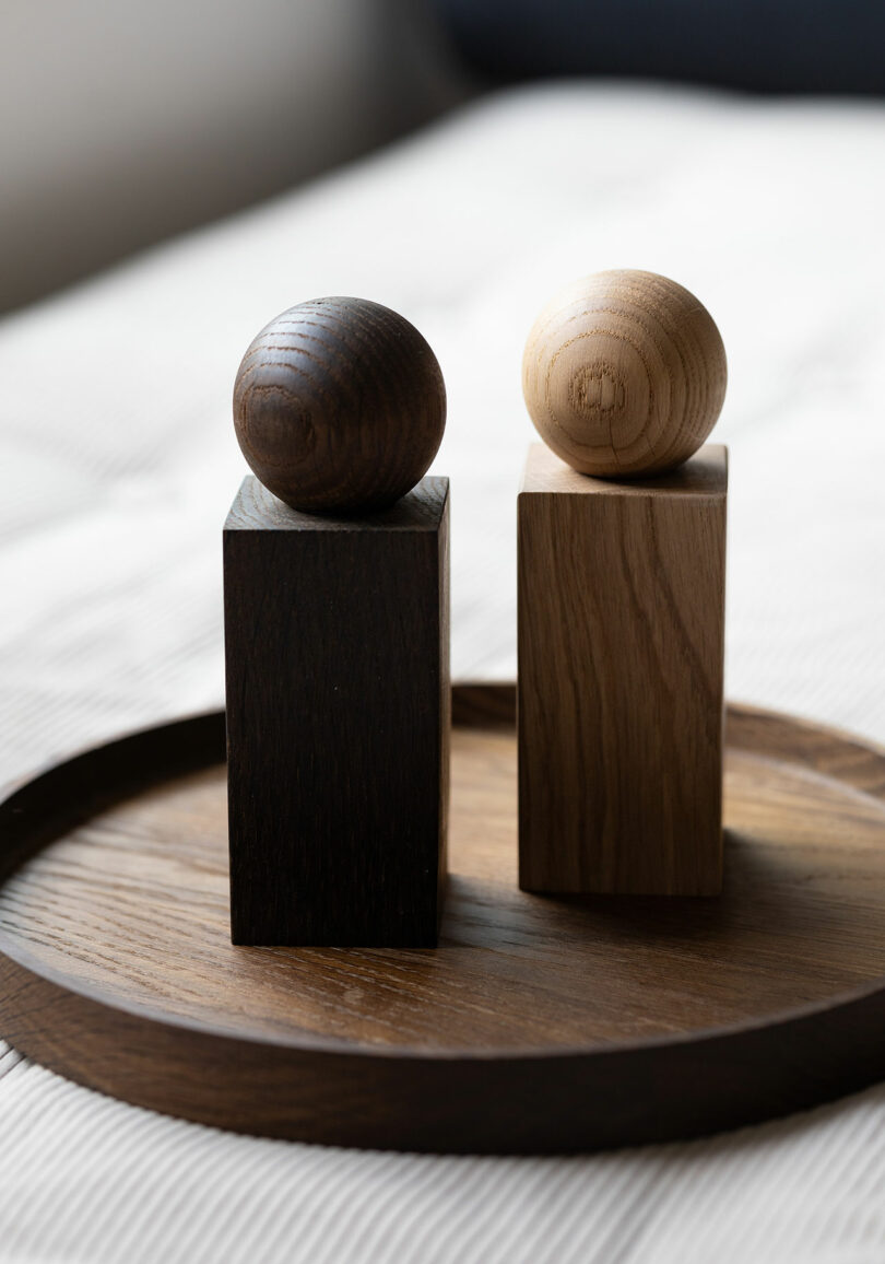 Close-up of a dark and light oak TWIST grinder standing on a wooden tray, showing their geometric rectangular bases and spherical tops.