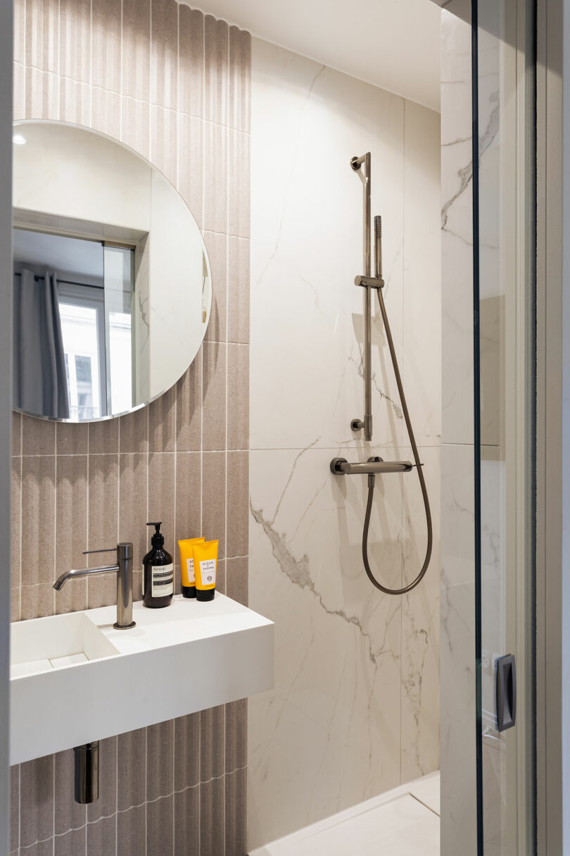 A modern bathroom featuring Carrara marble tiles, a round mirror, and a sleek rectangular sink.