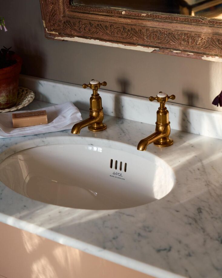 Detail view of Perrin & Rowe brass pillar taps on a honed Carrara marble countertop.