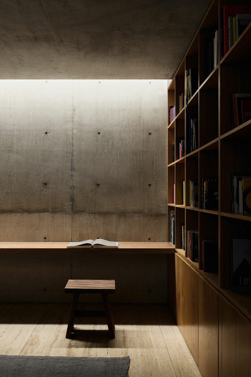 A minimalist wooden reading nook with built-in bookshelves and an open book.
