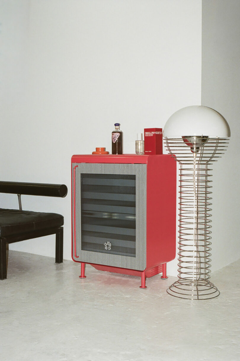 A red Rocco fridge with a ribbed glass door used as a bar cart with bottles on top.