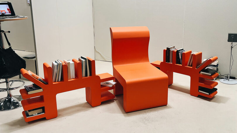 An orange modern chair featuring built-in wooden bookshelves on its sides.
