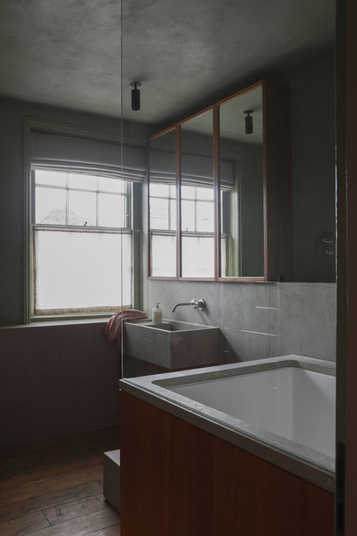 A green tadelakt and limestone bathroom with sapele wood accents around the tub.