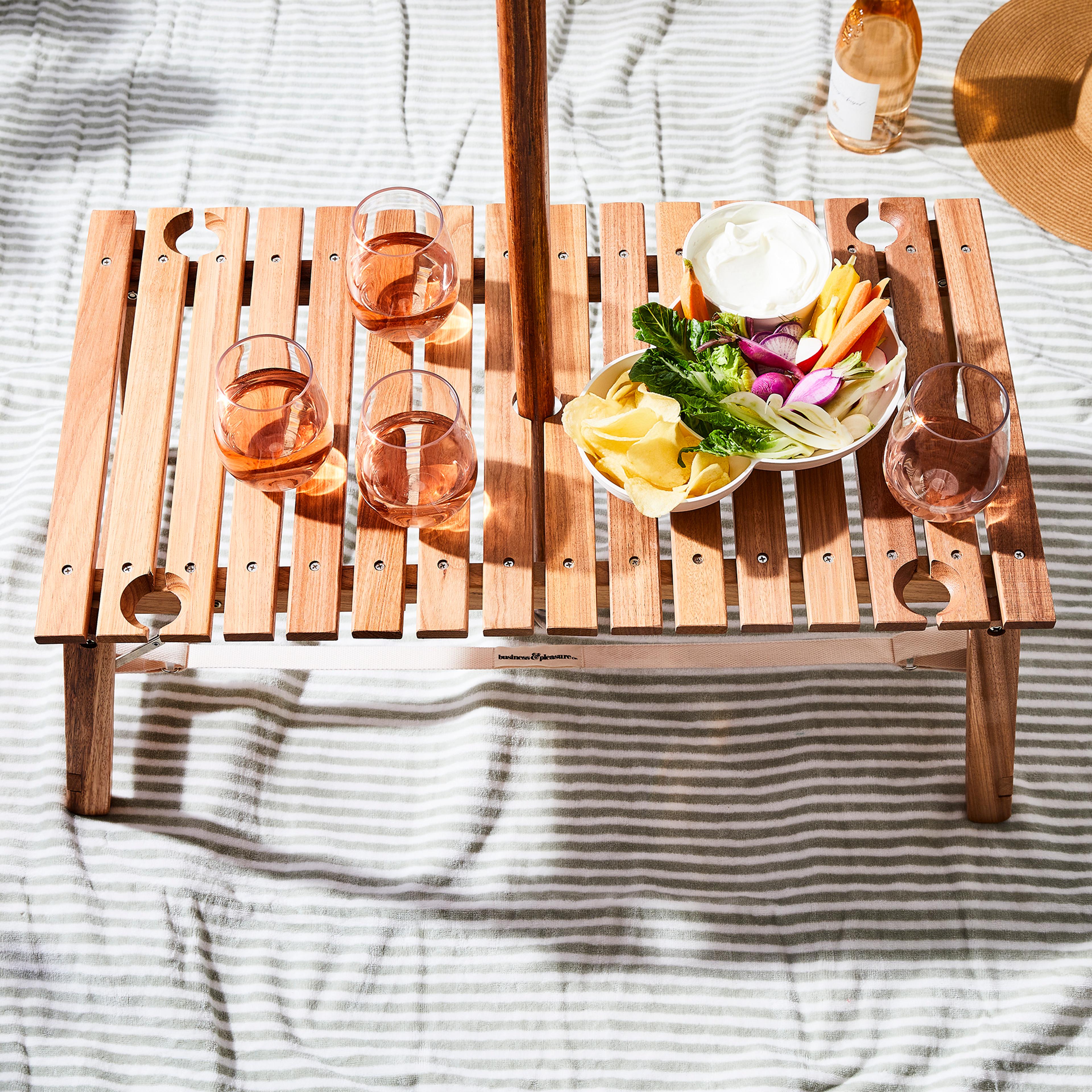 A small, portable wooden roll-up table sitting on grass with picnic items on top.