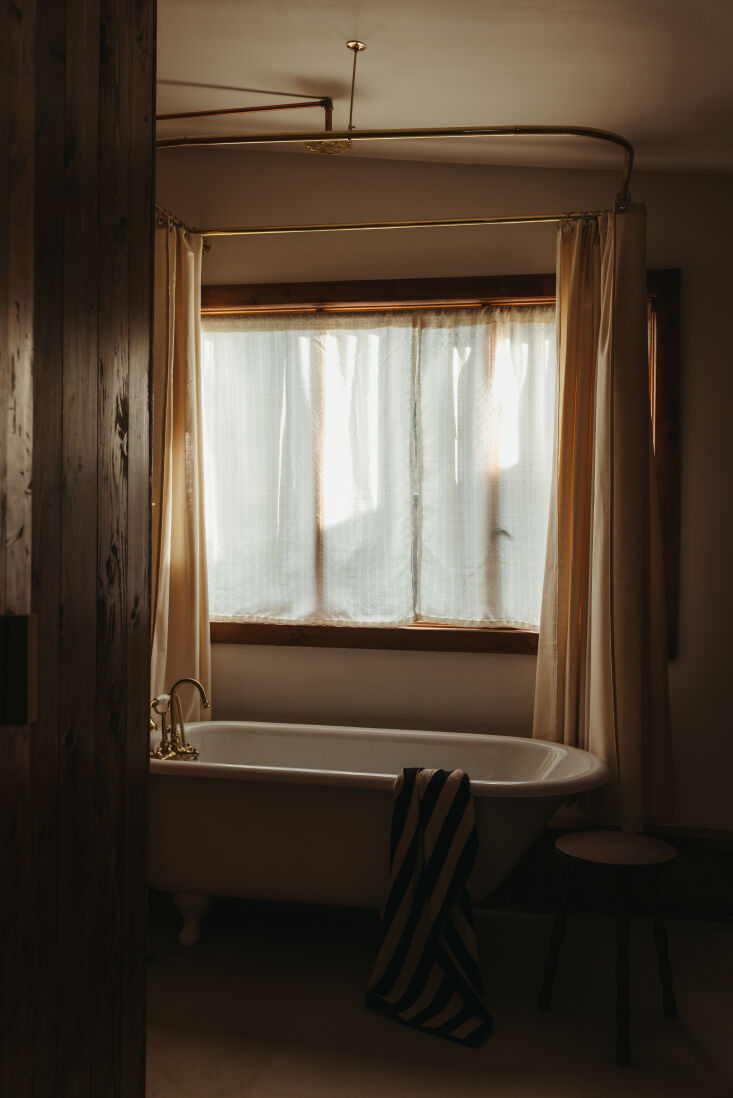 A restored 100-year-old cast iron clawfoot bathtub against a cedar-planked wall.
