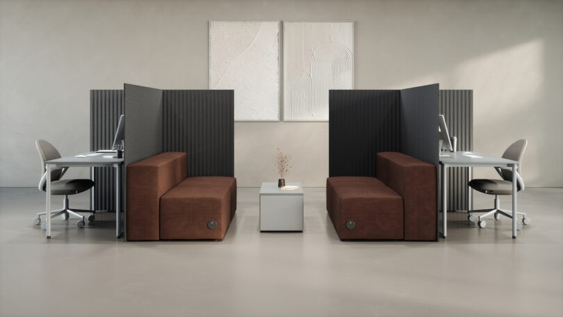 A minimalist office space featuring dark partition panels separating workstations and a central lounge area.