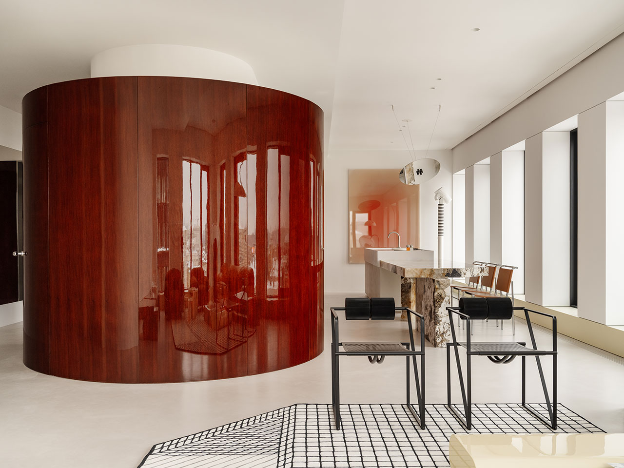 Open-plan living area with a curved glossy wood wall, marble kitchen island, and minimalist furniture.