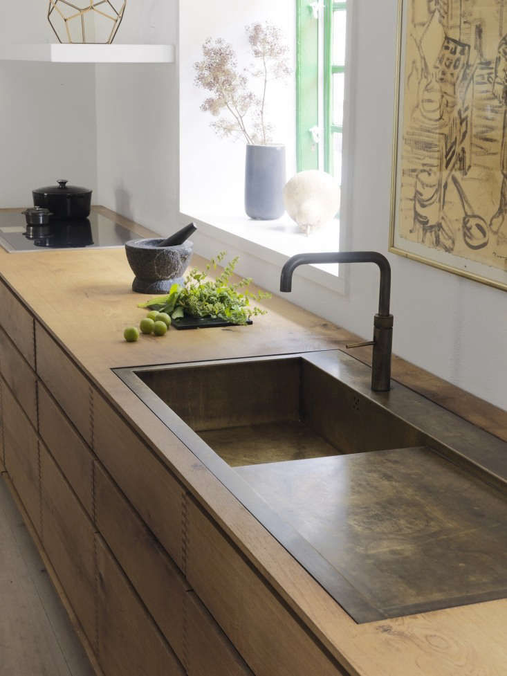 A weathered brass sink integrated into a light wood countertop.
