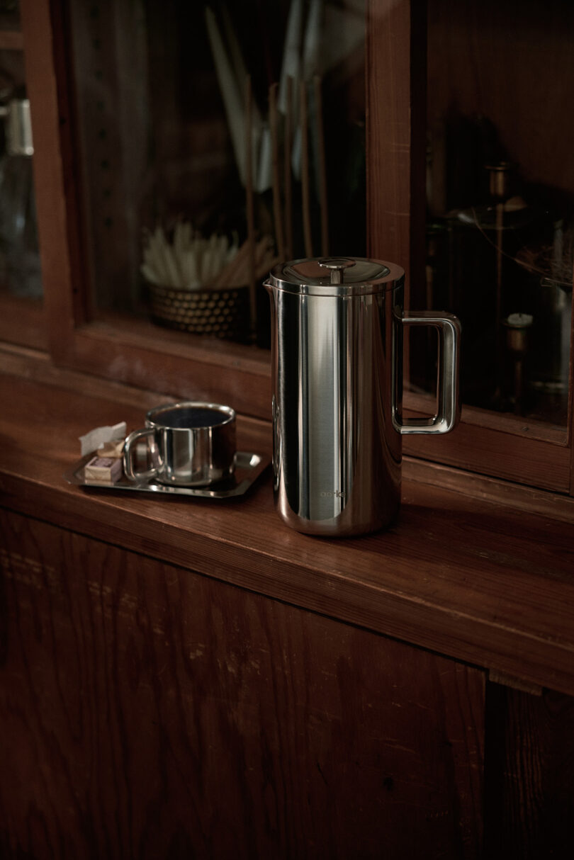 The Aarke Coffee Press and a matching metal cup sitting on a rustic wooden countertop.