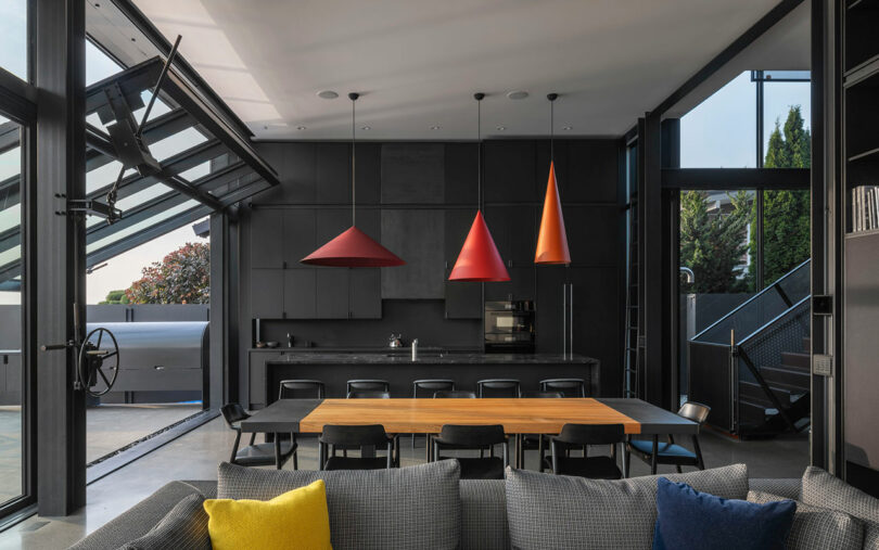 Modern open-plan kitchen and dining area with black cabinetry and three geometric red pendant lights.