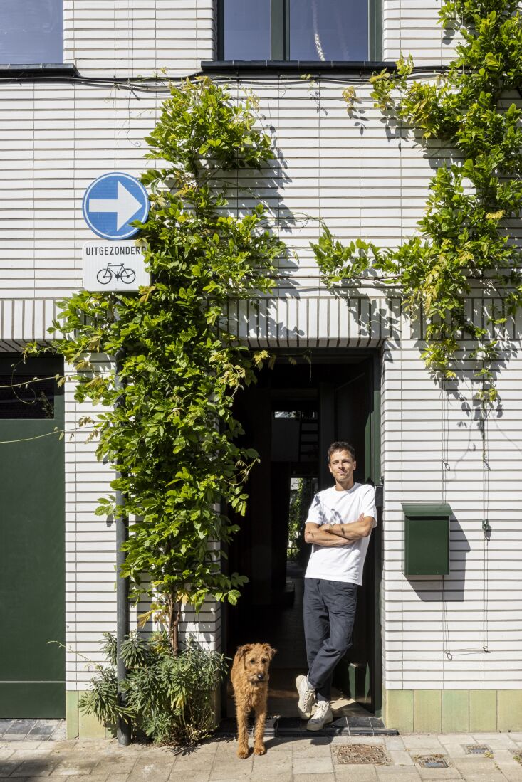 A man standing by a doorway with a dog, surrounded by climbing wisteria plants.
