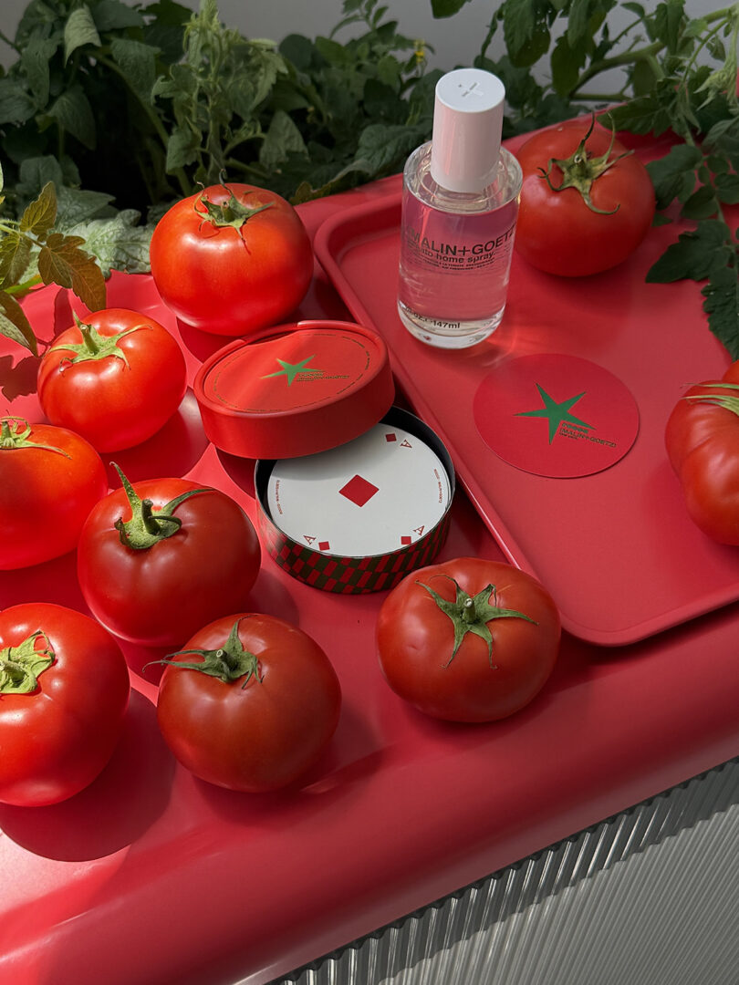 A MALIN+GOETZ bottle arranged with tomatoes and red lifestyle items.