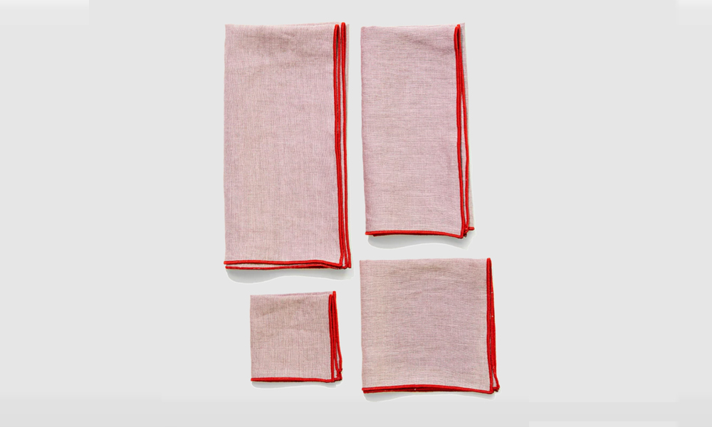 A set of Oyster-colored napkins featuring red stitching on pink linen.