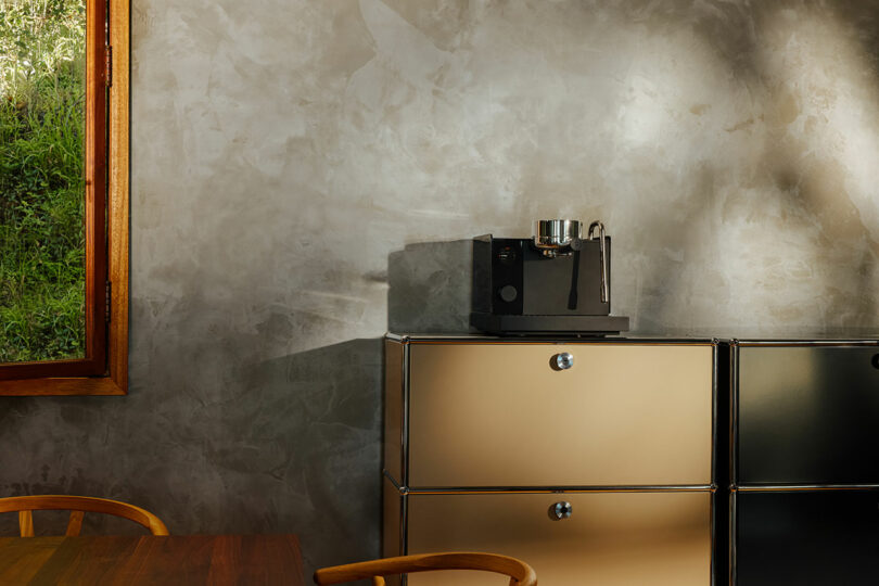 A black Fellow espresso machine in a modern, minimalist kitchen setting with concrete walls and wooden accents.