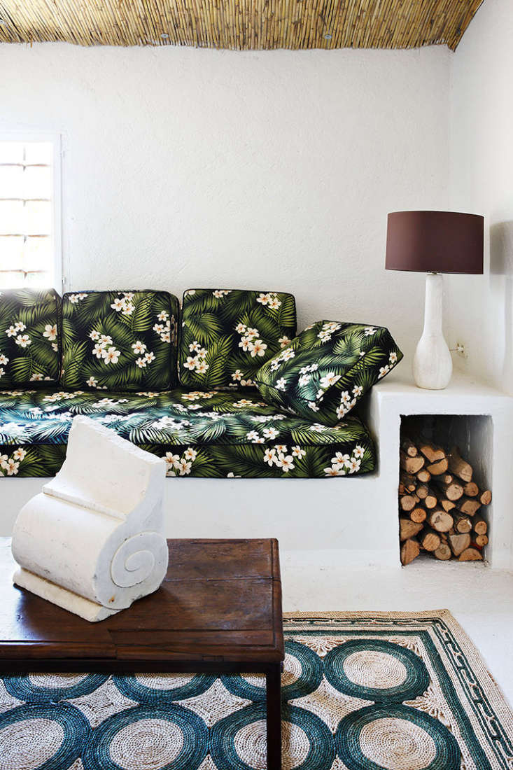 A rustic built-in bench with floral cushions and an open space underneath filled with firewood logs.