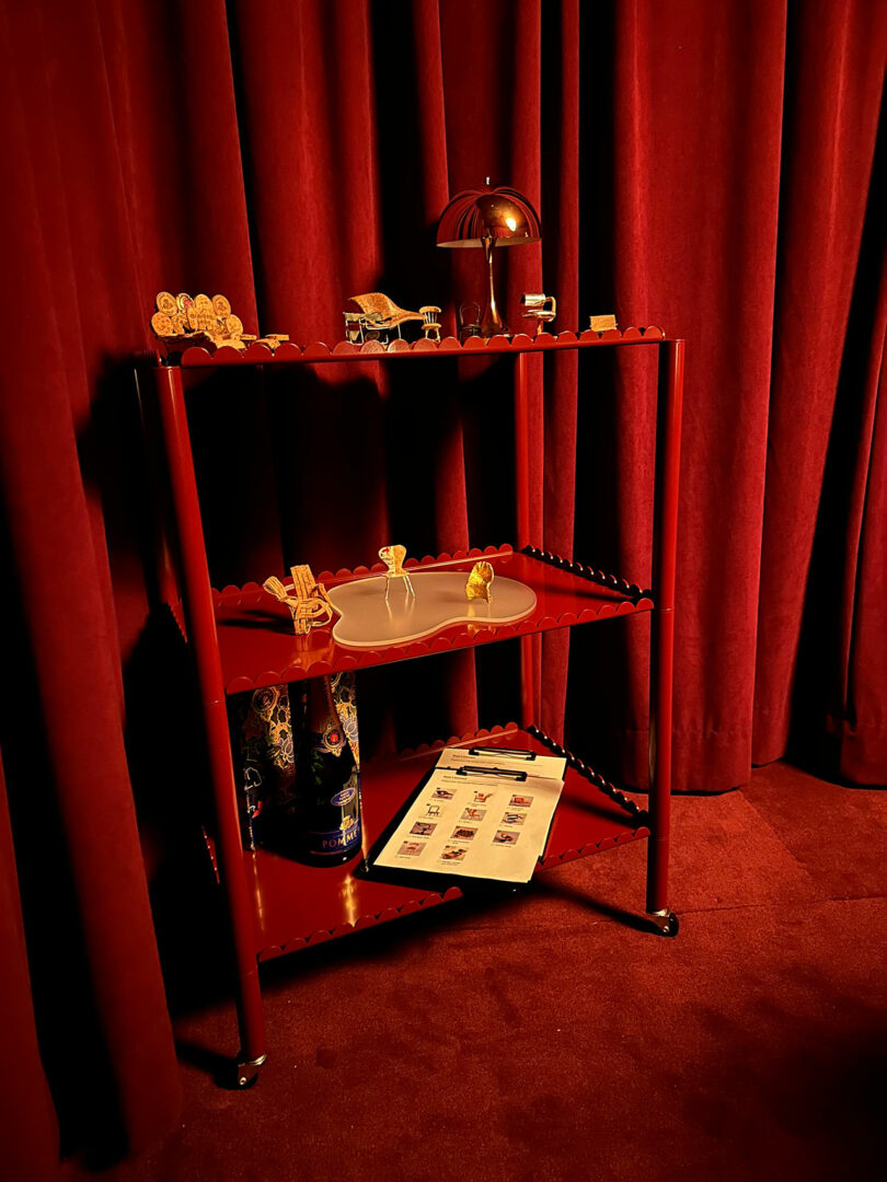 A red metal shelf with various objects, including a miniature champagne chair.