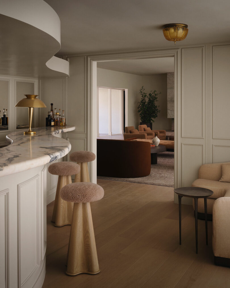 A curved marble bar with gold accents and plush barstools in a modern OSKLO-designed interior.