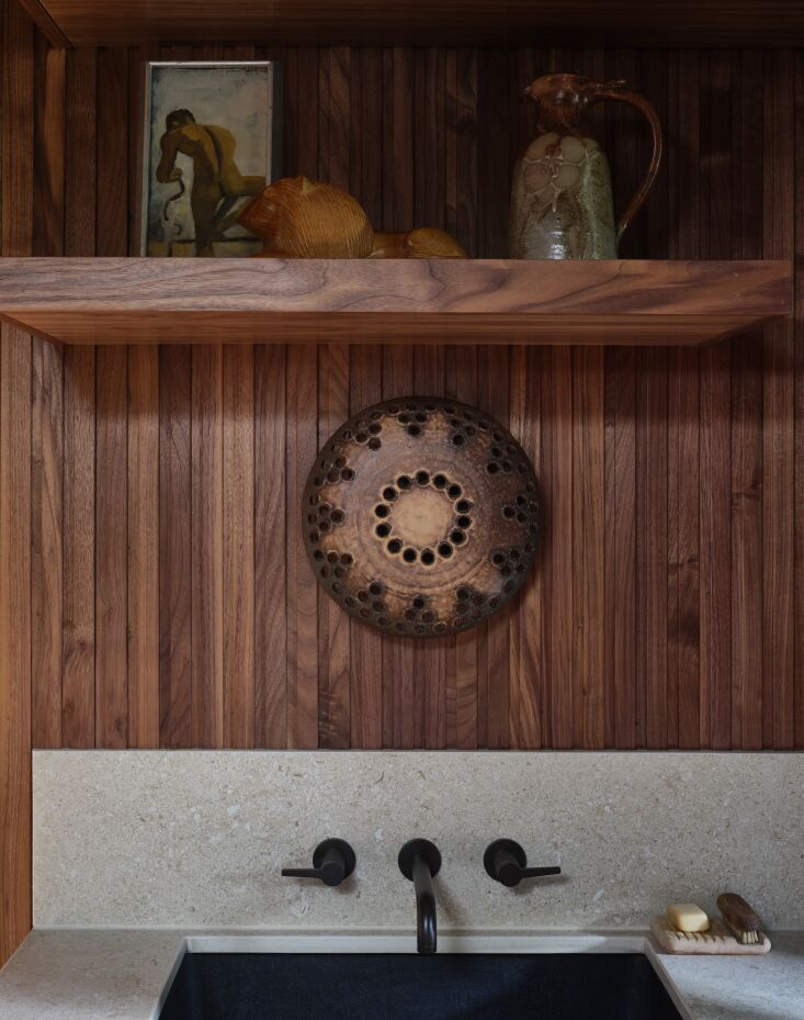 Close-up of an Avorio Dekton counter with wall-mounted brass faucets and a vintage ceramic sconce.