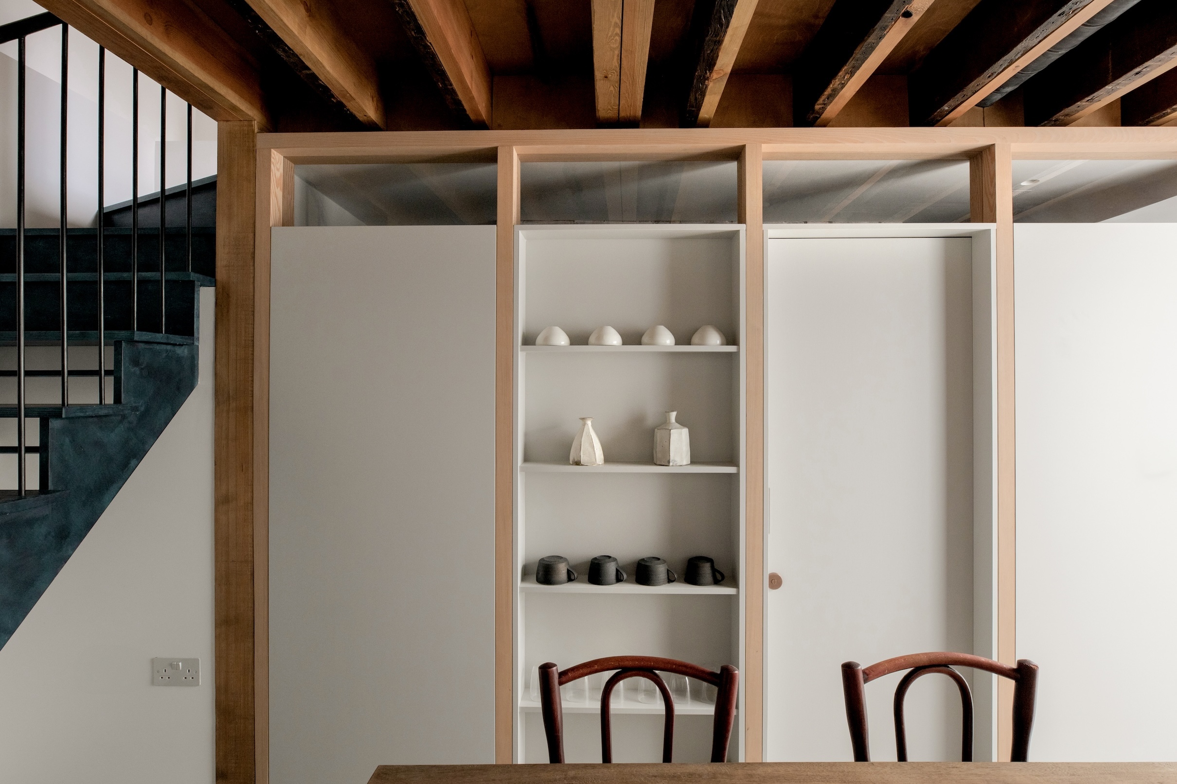 A partial wall with built-in display shelves serving as a soft divide between a kitchen and office.