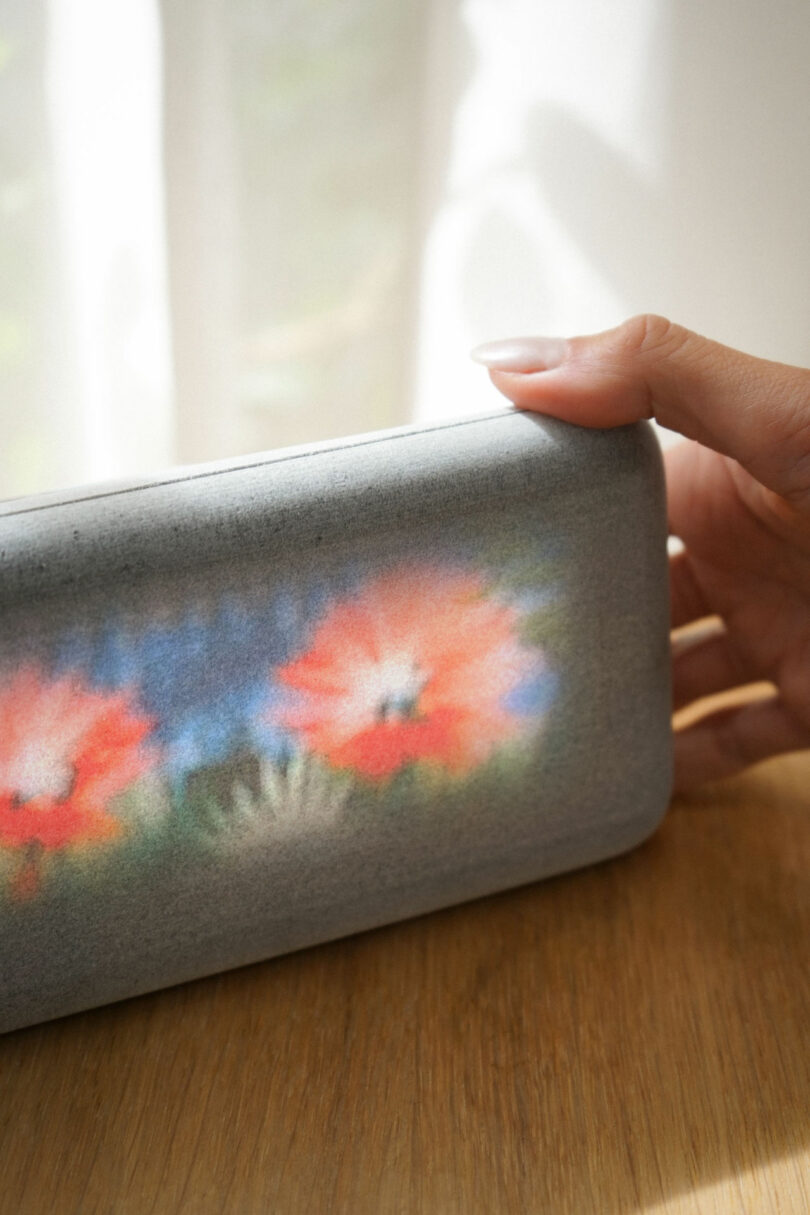A person holding the gray, 3D-printed Dream Recorder showing a blurred floral image on its screen.