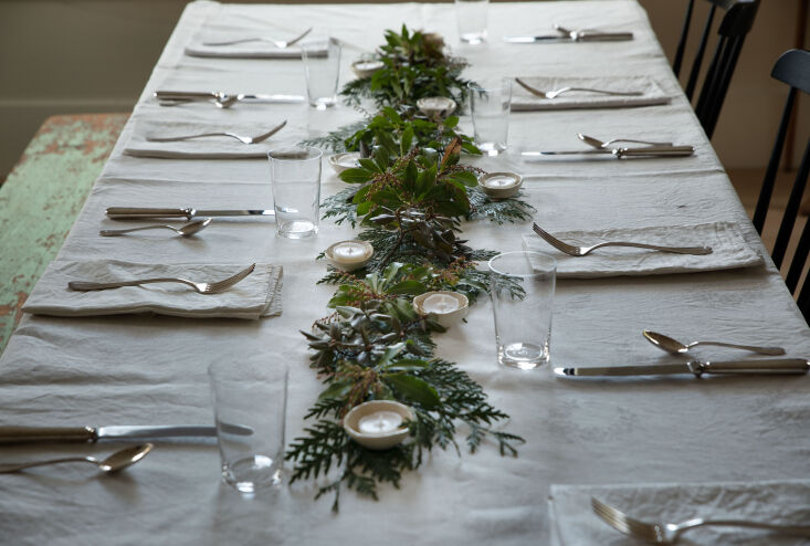 Handmade ceramic votives nestled among foraged evergreen branches on a table.