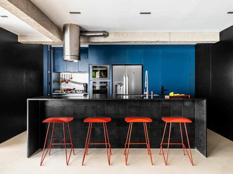 Modern kitchen with a black island, red barstools, and exposed concrete architectural elements.