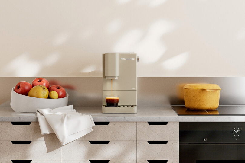 A cream-colored espresso machine brewing coffee on a kitchen counter near an induction stove.