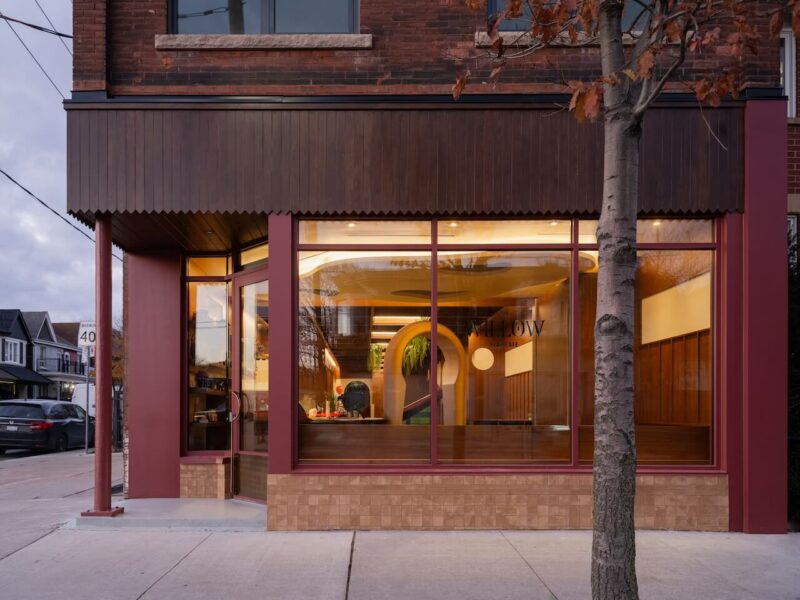 Exterior street view of The Willow Play Cafe featuring large windows and warm interior lighting in a Toronto neighborhood.