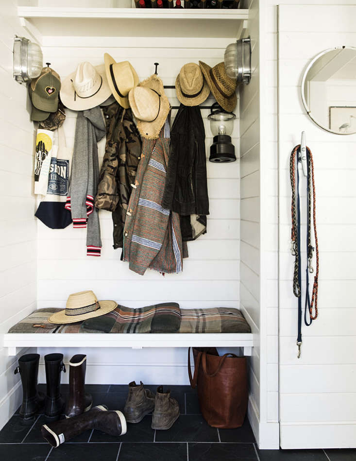 A mudroom with a porthole mirror, nautical cleat door handles, and industrial sconces.