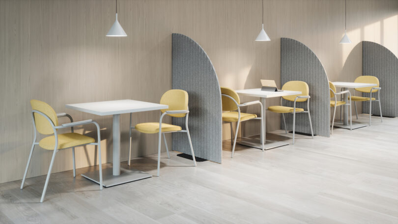 A row of modern desks with yellow chairs separated by grey acoustic privacy dividers.