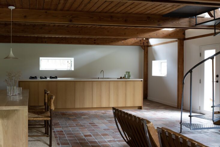 A long, honey-stained oak kitchen island with a limestone countertop and minimalist fixtures.