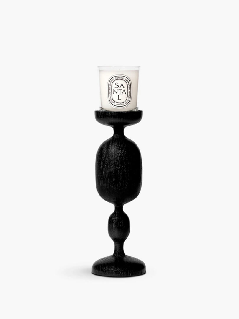 An intricately shaped black ceramic candle holder with a white luxury candle.