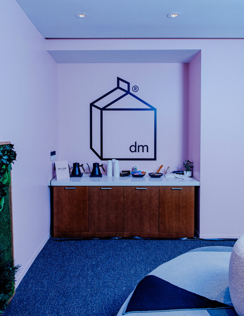 A stylish office refreshment station with tea kettles and snacks against a soft pink wall.