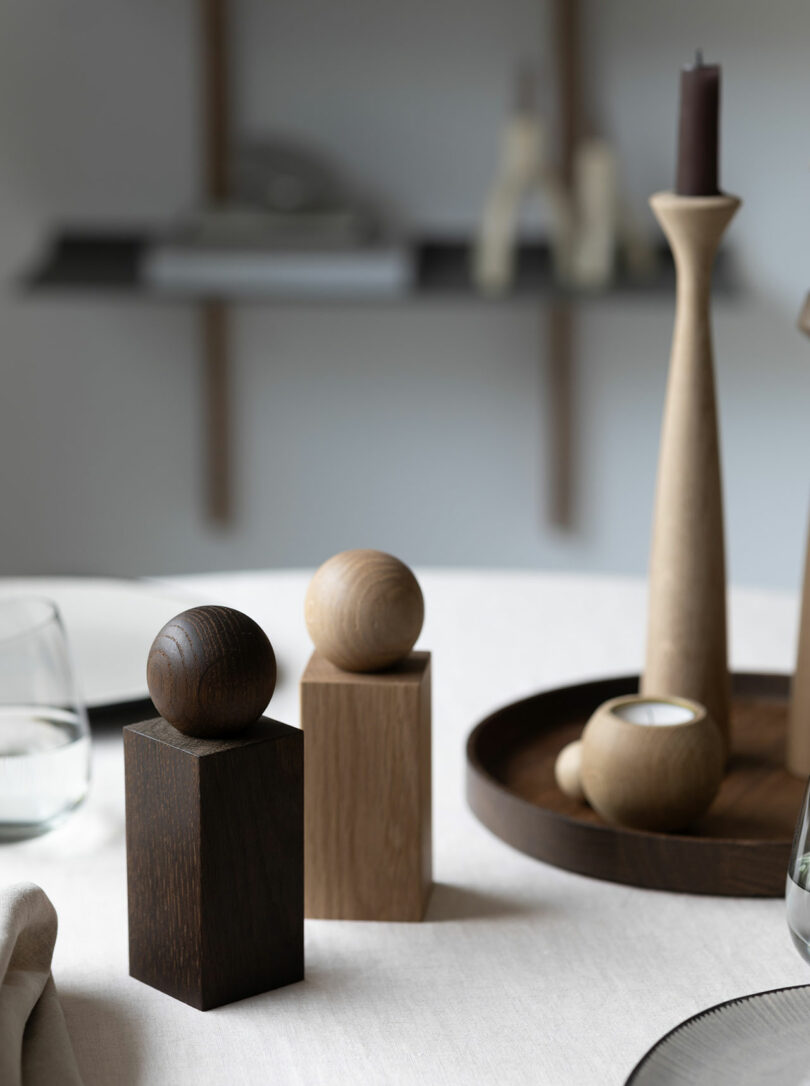 Two wooden TWIST grinders on a dining table with a blurred background showing home decor on a shelf.