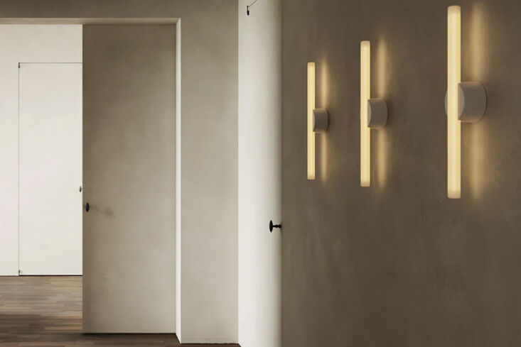 A minimalist brass Tala Kilter wall light mounted vertically on a wall.