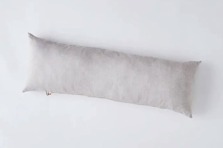 A Celina Mancurti linen body pillow featuring a distinct brass zipper and leather pull detail.