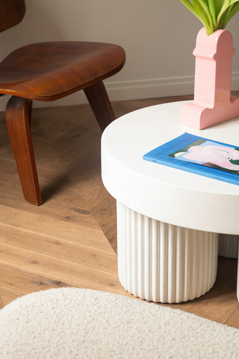 A round white dining table paired with a mid-century wooden chair on a herringbone wood floor, illustrating curved furniture in a linear space.