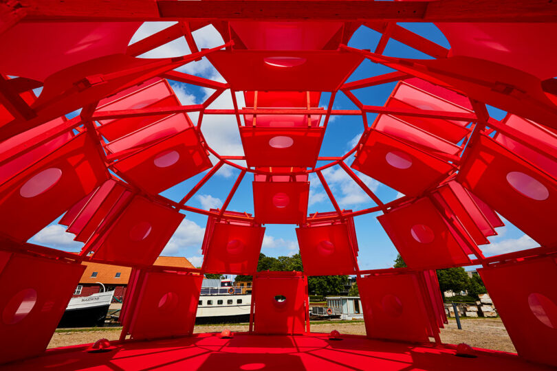 View from inside the red geometric structure looking out at the Copenhagen sky and surrounding trees.