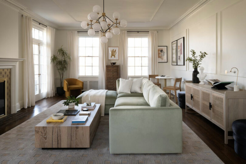 Modern living room with a green sectional sofa, wooden coffee table, and large windows with natural light.