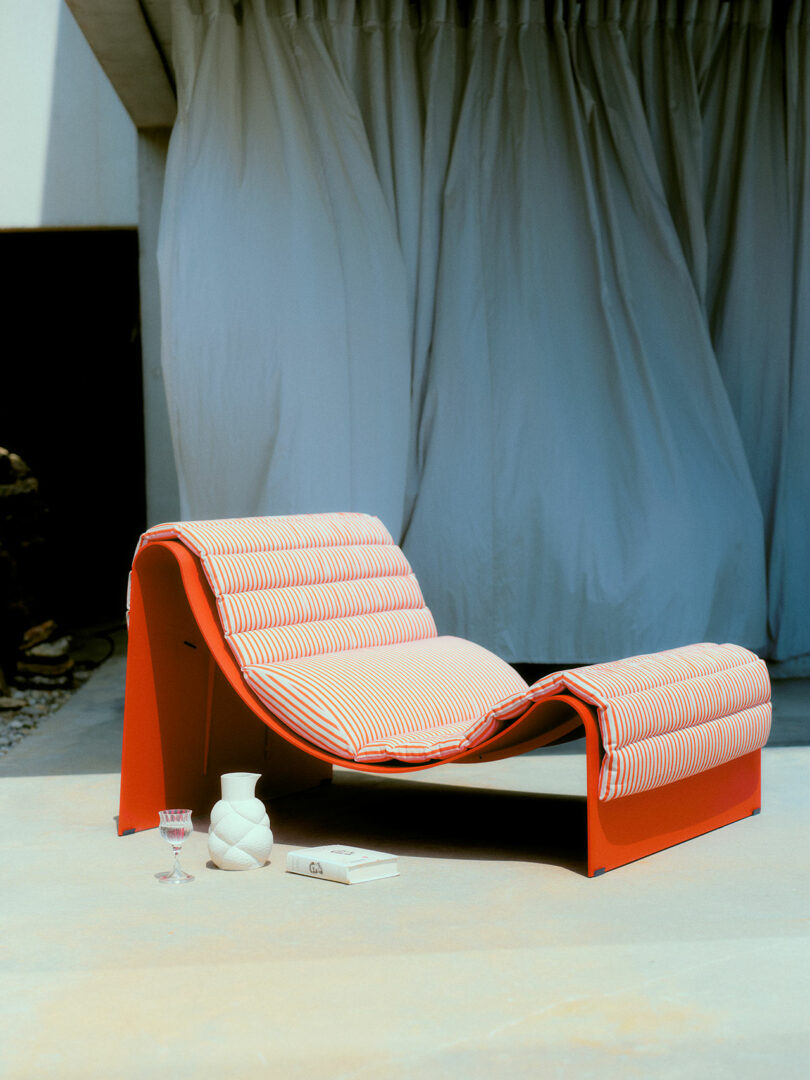 A modern red lounge chair with striped cushions and matching footrest on a concrete patio.