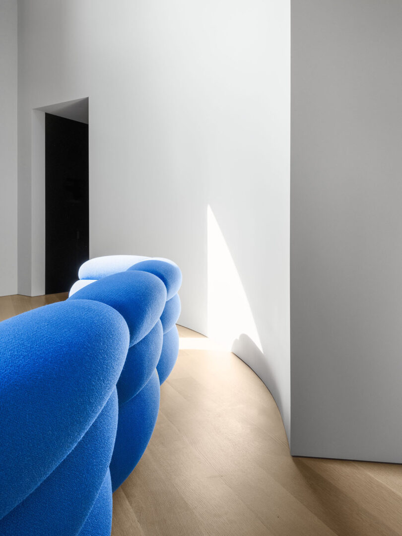 Blue sculptural sofa in a minimalist room with natural light hitting the light wood floor.