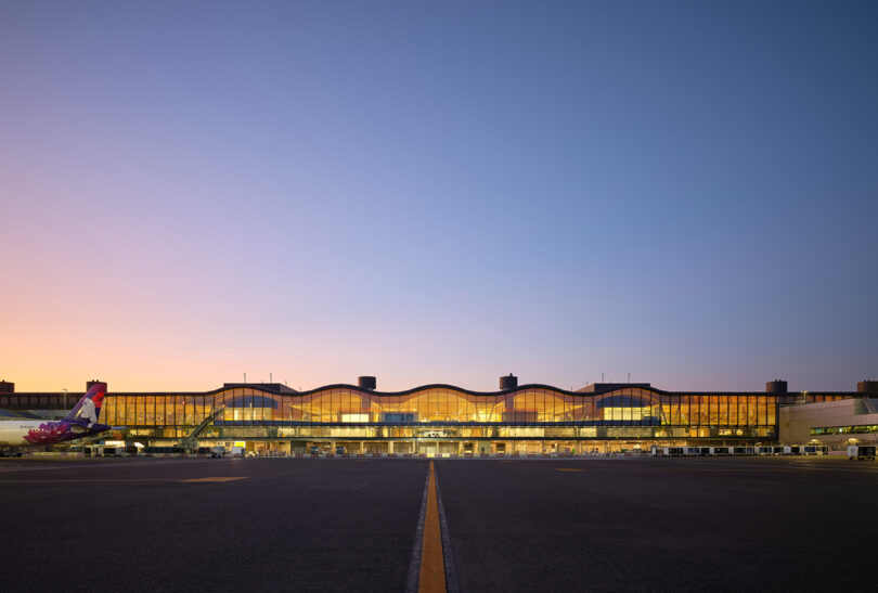 Exterior view of the illuminated PDX terminal at dusk with a plane on the tarmac.
