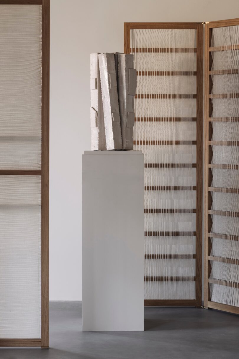 A white abstract ceramic sculpture on a pedestal next to textured wooden room dividers.