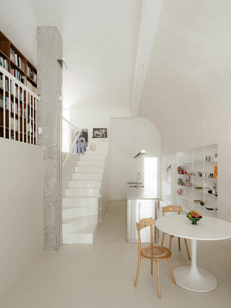 Minimalist kitchen and dining area with a white staircase leading to a loft library in a Madrid conversion.