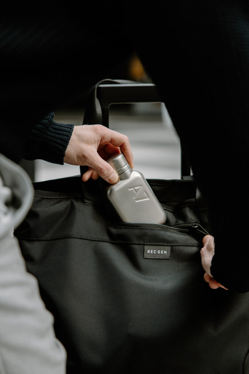 A small silver memobottle being tucked into the external pocket of a black bag.