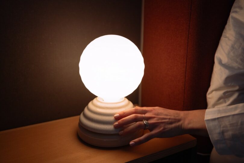 A hand interacting with a glowing lamp in a dark room with warm red ambient tones.