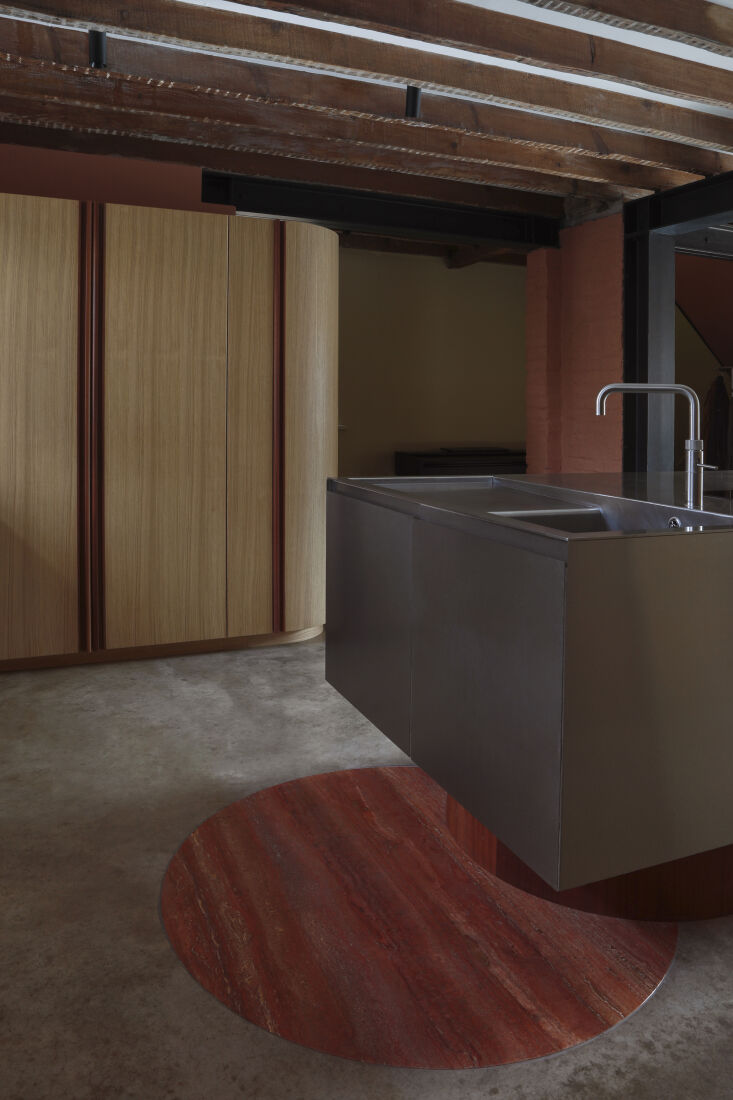 A circular red travertine floor inlay next to a wooden kitchen island.
